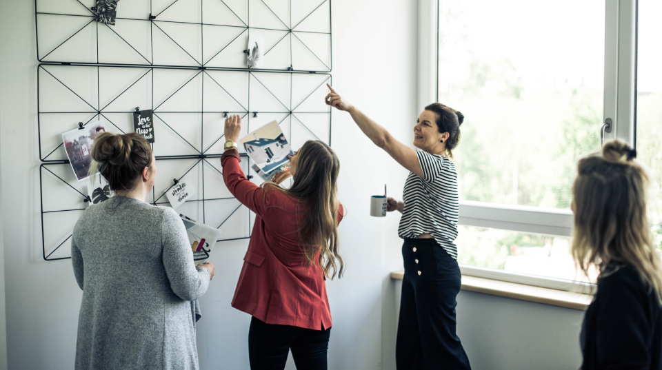 4 Frauen hängen Bilder an einer Wand auf